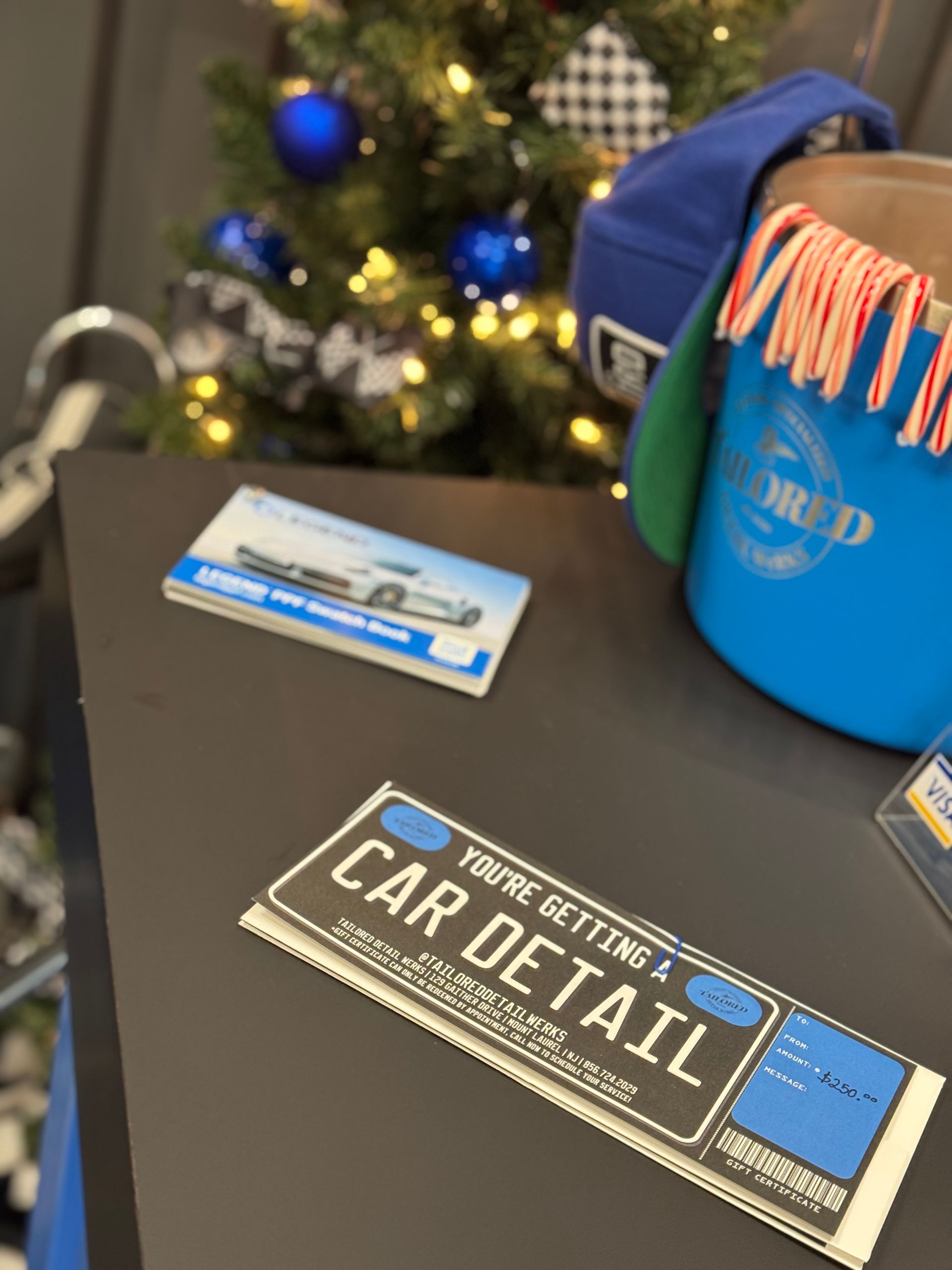 Car detail business cards on a table beside a blue bucket and blurred holiday decor.