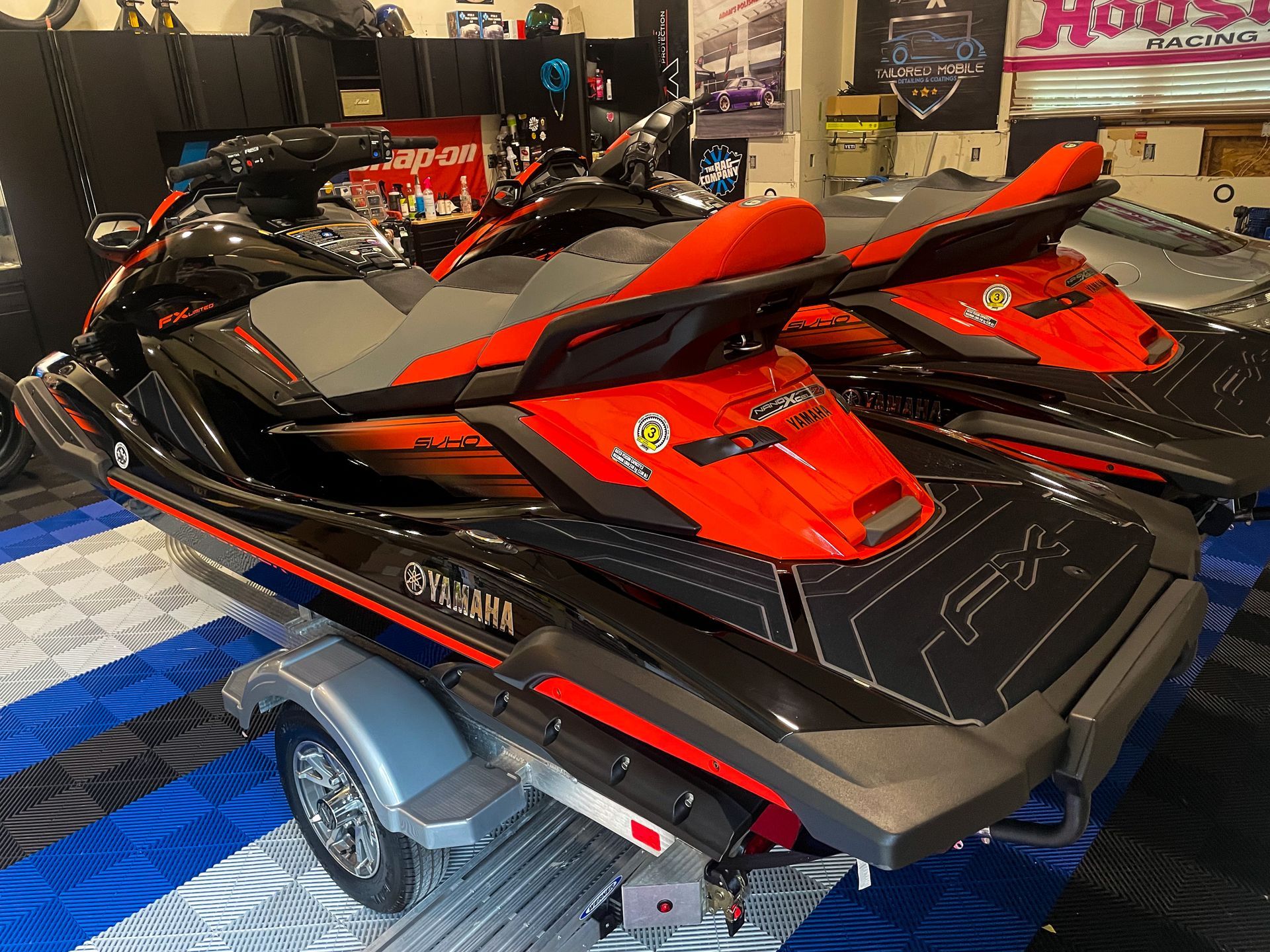 Red and black jet skis displayed on a trailer at an indoor showroom.
