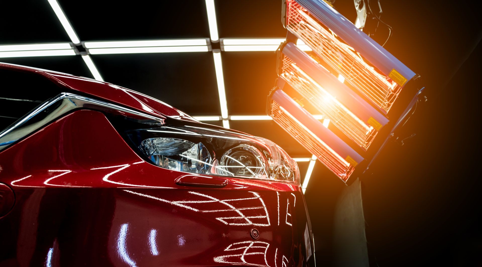 Red sports car under bright orange lights in a dark showroom or garage
