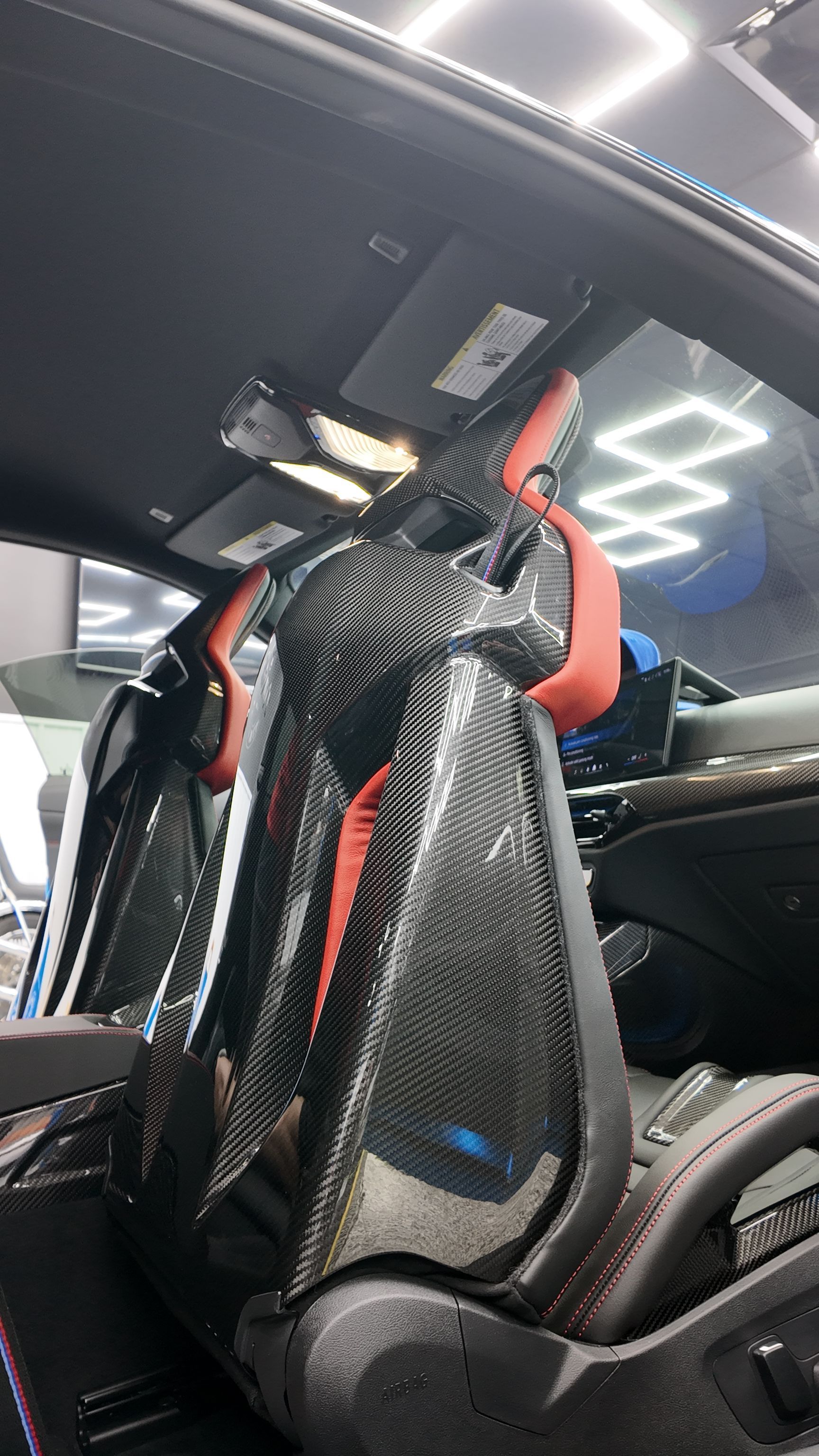 Black carbon-fiber racing seat with red accents inside a car interior, viewed from the open door