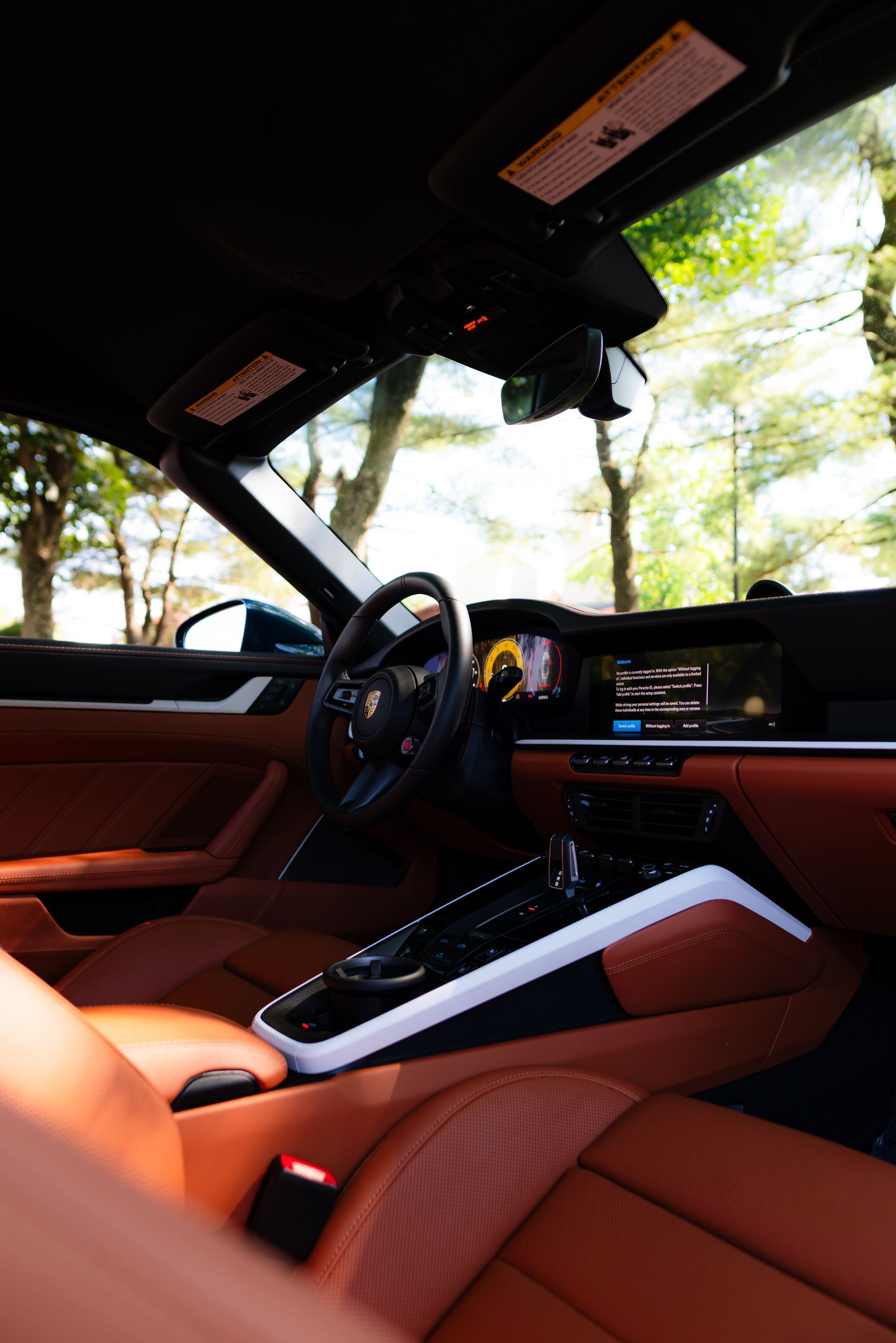 Luxury car interior with orange leather seats, steering wheel, and dashboard, parked near trees in daylight