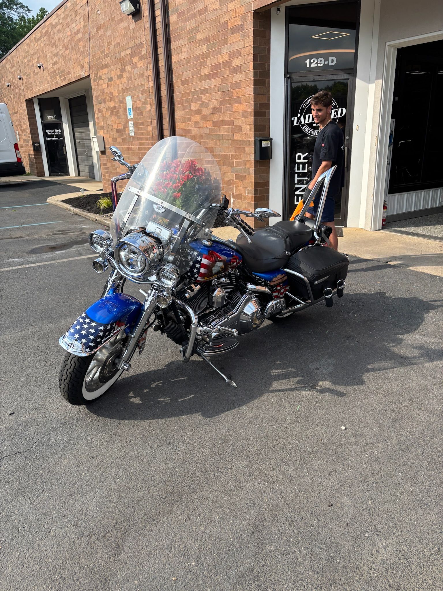 Blue and black motorcycle parked outside a brick building, with a rider standing nearby.