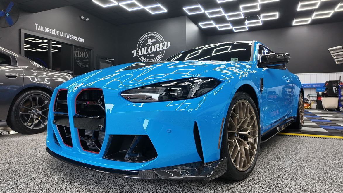 Bright blue BMW sports car displayed indoors at an auto shop, front view with black grille and bronze wheels