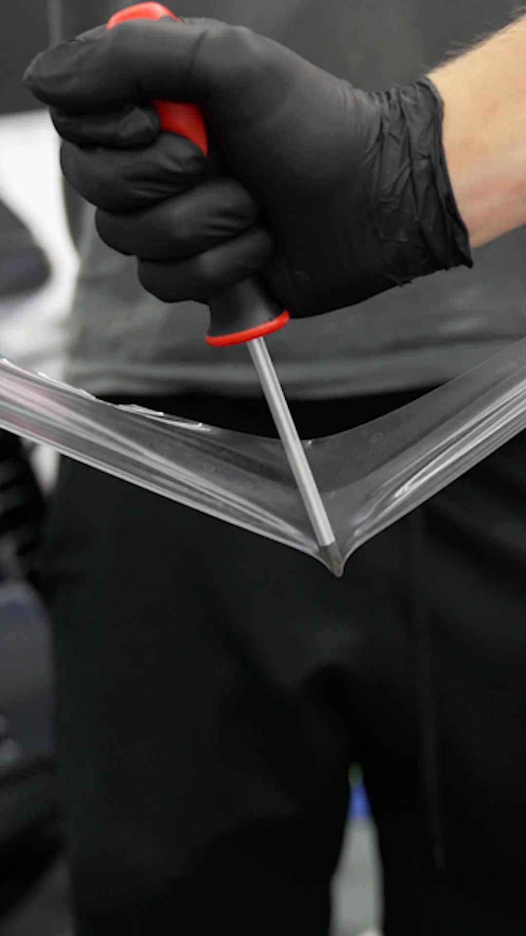 Gloved hand using a screwdriver to pry open the seam of a black case or container
