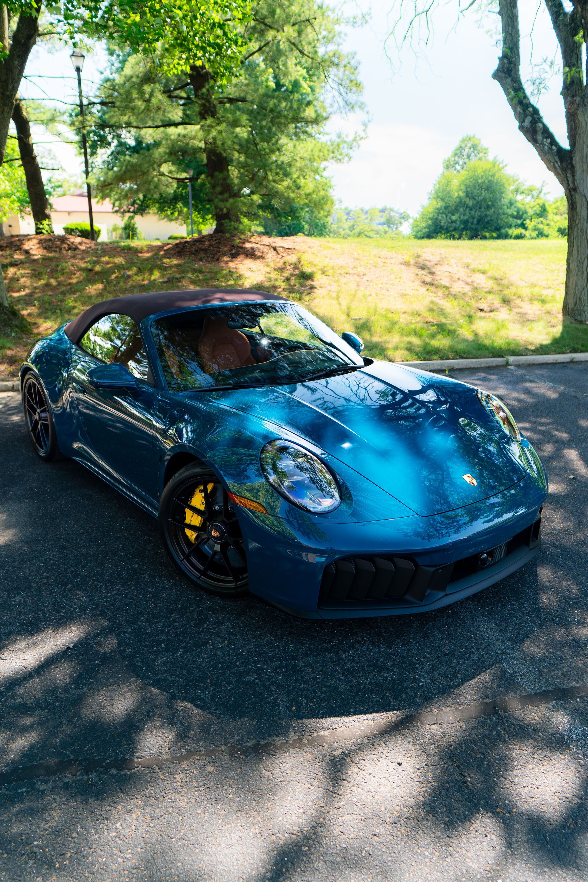 Blue sports car parked on a tree-lined road in dappled sunlight
