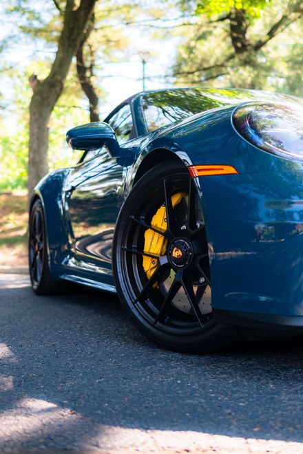 Blue sports car with black wheels parked on a sunlit tree-lined road