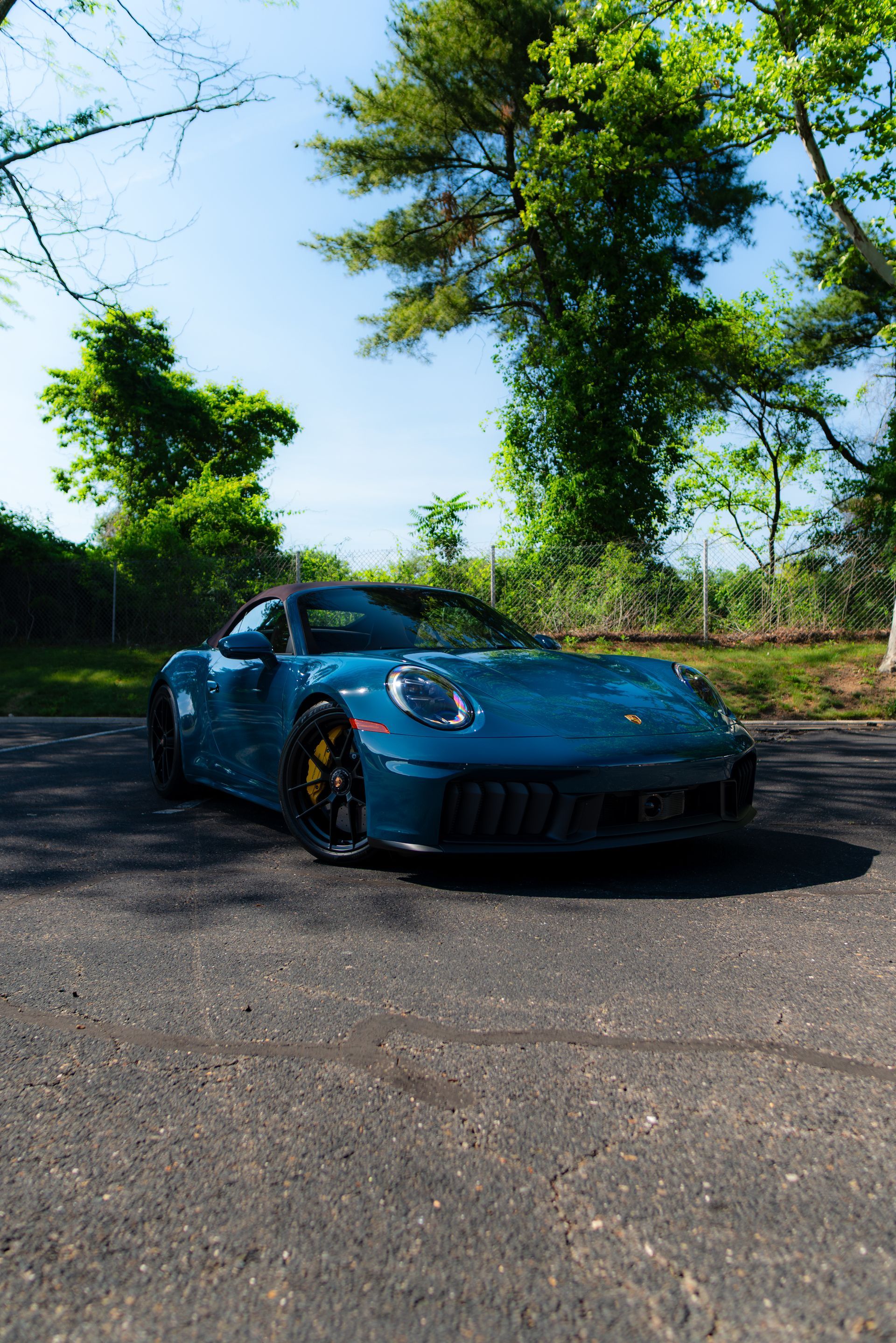 Blue sports car parked on a sunlit road surrounded by green trees and clear sky