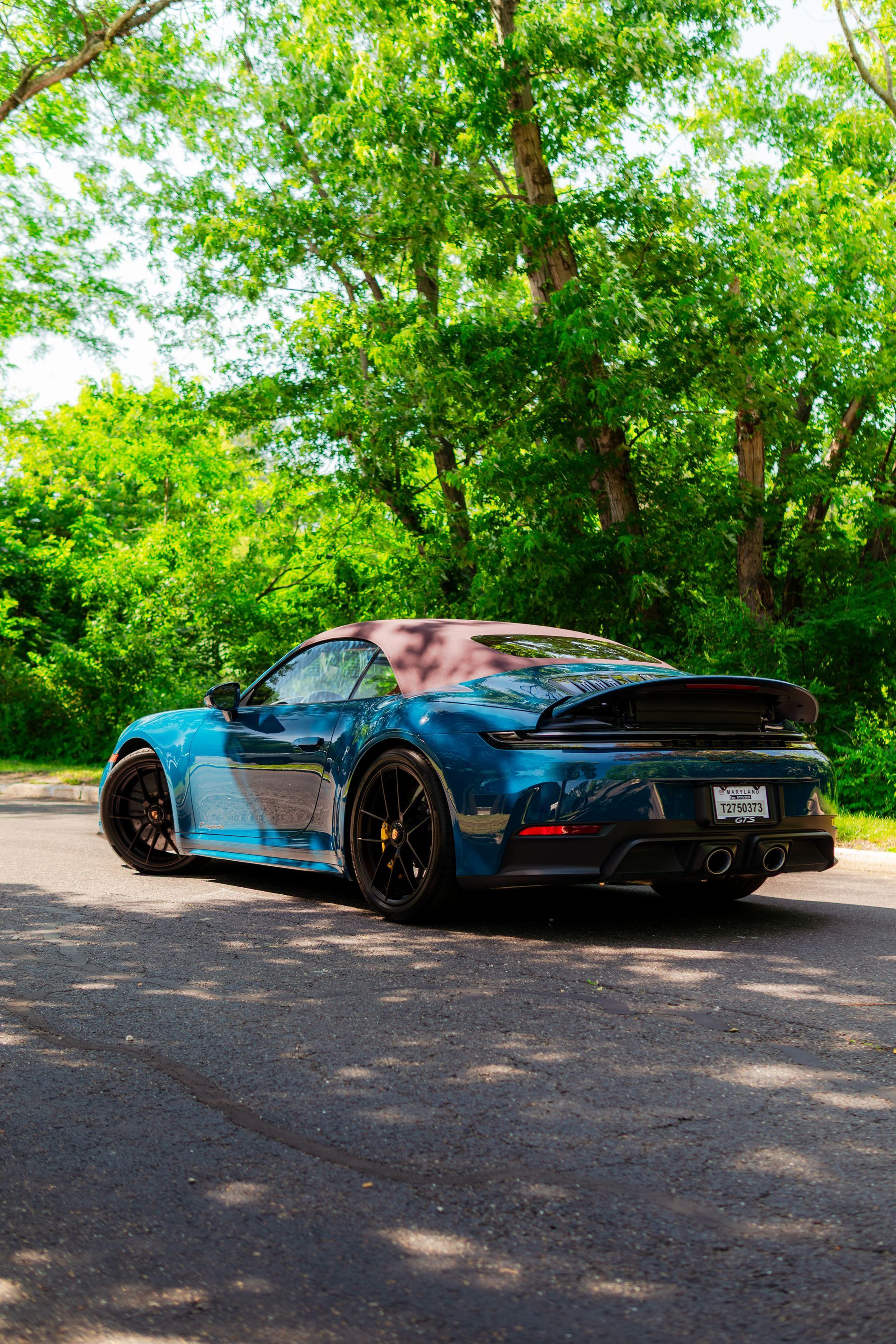 Blue sports car parked on a tree-lined road in bright sunlight