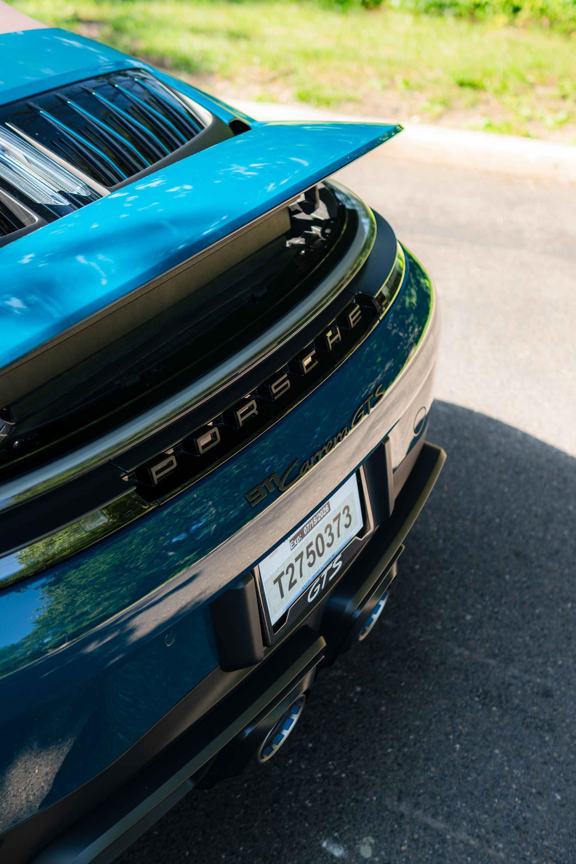Close-up of a blue Porsche rear with spoiler and license plate on a sunlit road