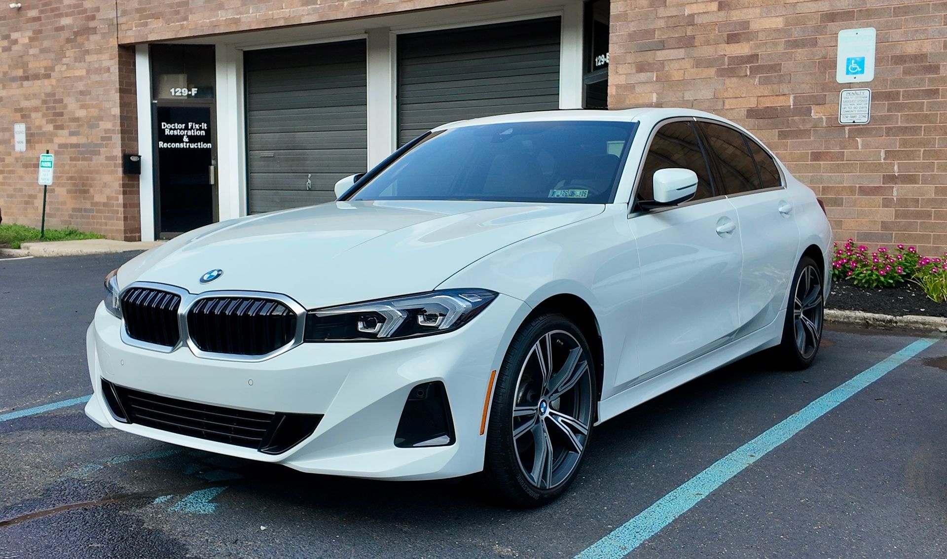 White BMW sedan parked in front of a brick building with a garage door