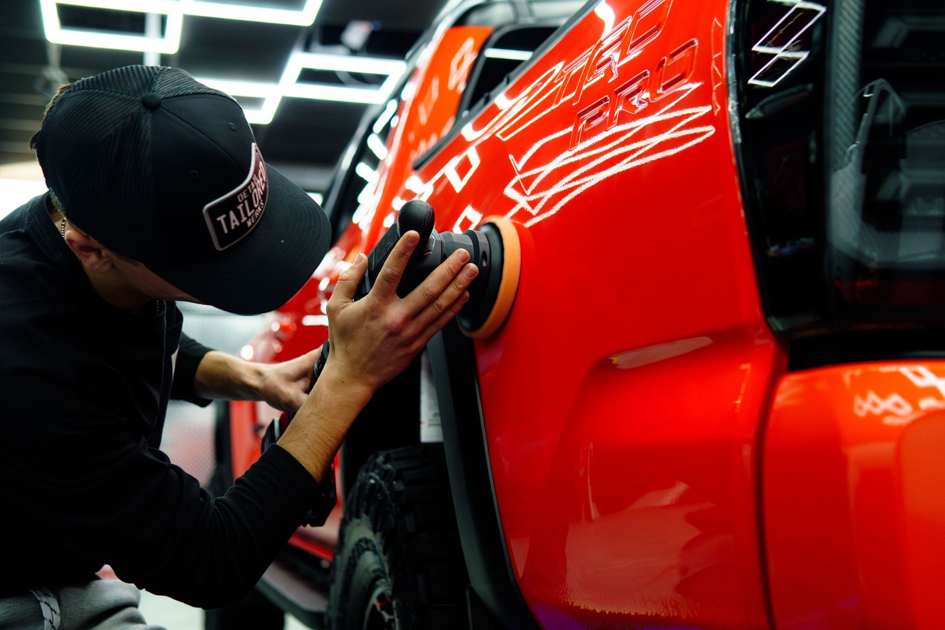 Mechanic polishing a red car door in a garage, with bright overhead lights.