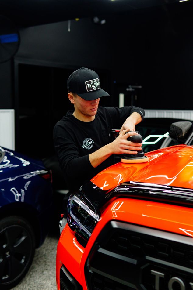 Person detailing an orange car beside a dark blue vehicle in a garage
