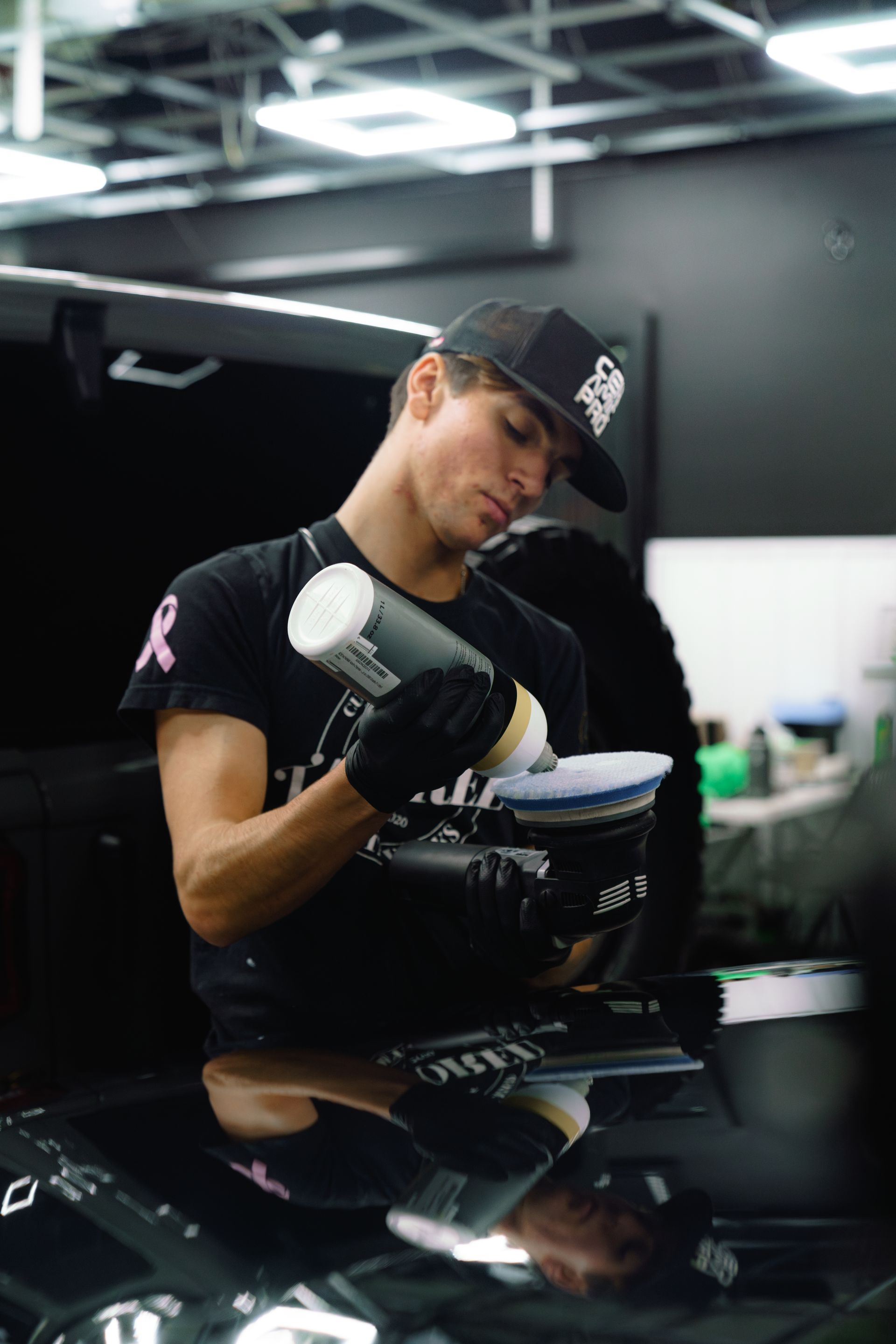 Mechanic in black gloves inspecting a white car panel in a dim garage