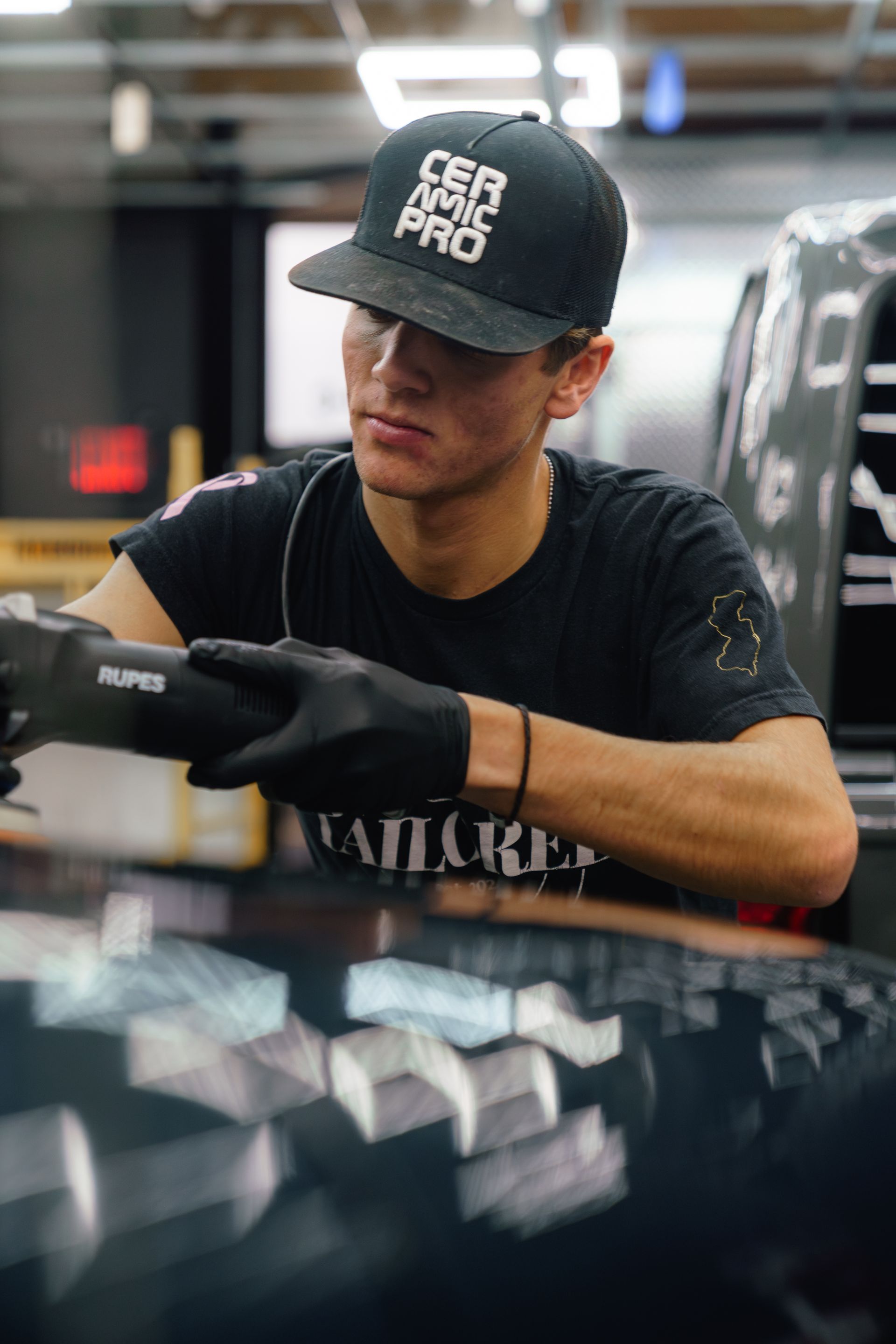 Gloved worker in a black cap polishing a car in a garage