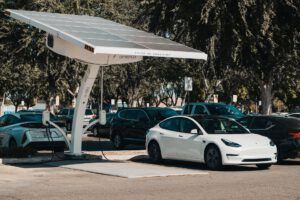 White Tesla parked under a solar canopy in a parking lot.