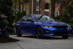 Blue sports sedan parked in a driveway in front of a house