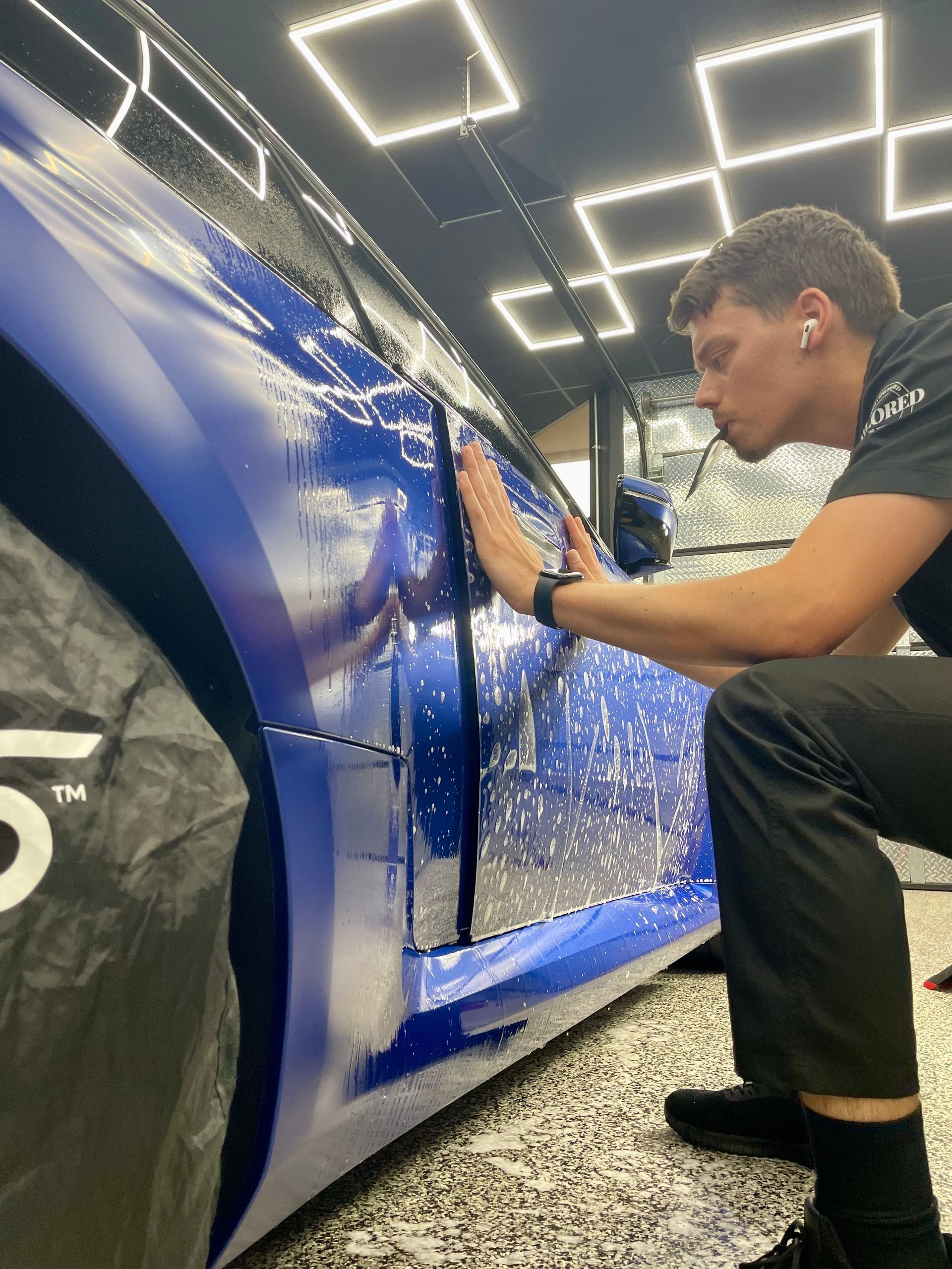 Young man polishing a blue sports car in a brightly lit garage