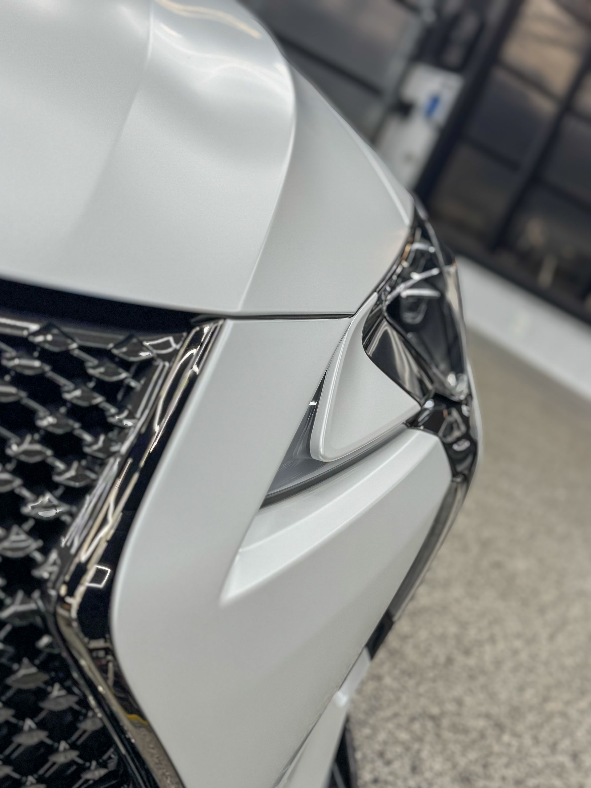 Close-up of a white car’s front corner and headlight with a chrome grille