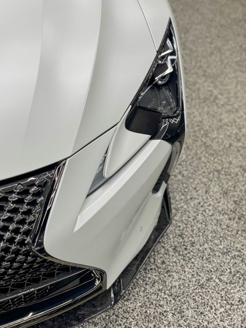 Close-up of a white sports car front bumper with black mesh grille and angular headlight detail