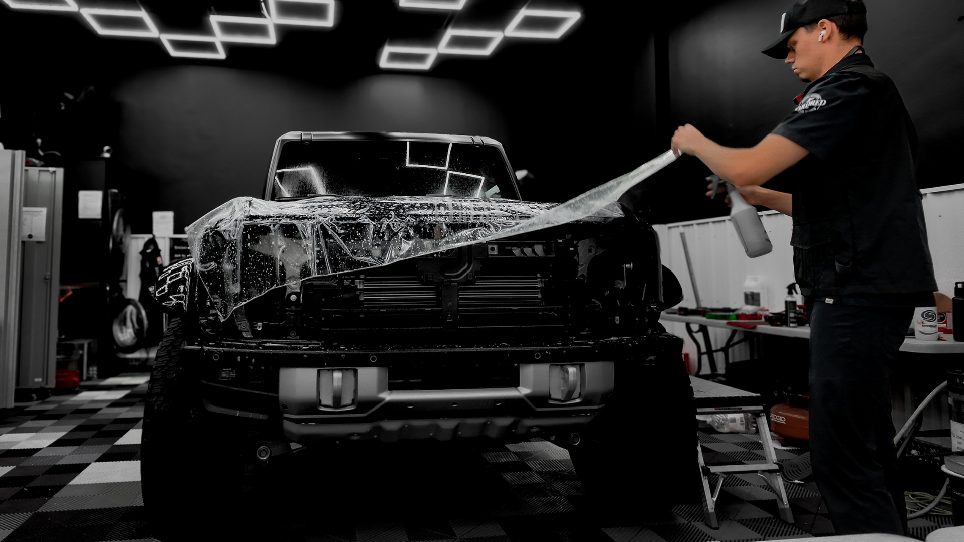 Detailer washing a black pickup truck with a pressure hose in a car wash bay