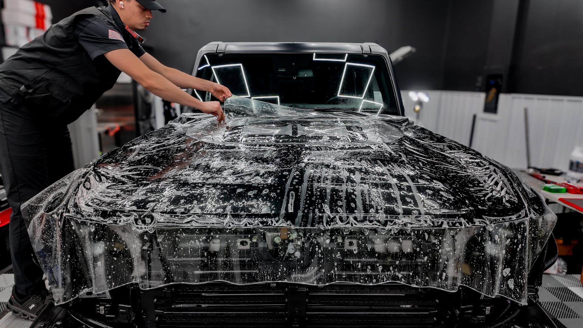 Person washing a black car with thick soap foam in a garage-like setting