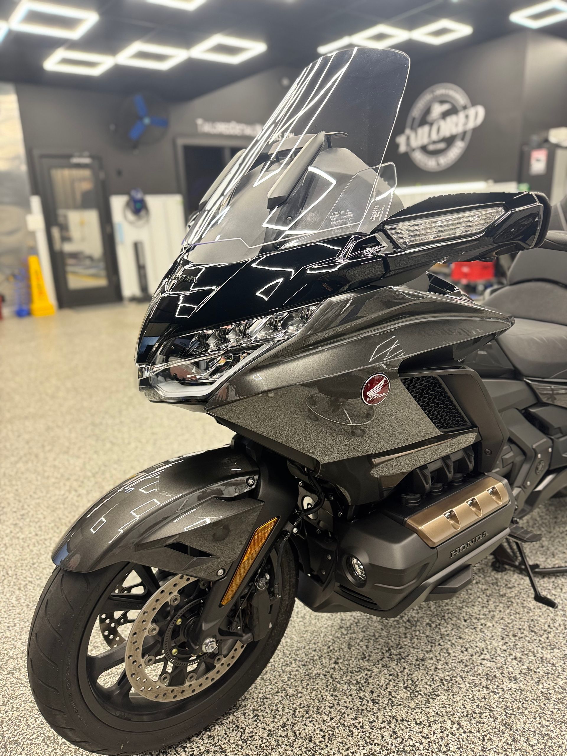 Black touring motorcycle with tall windshield, parked indoors on a showroom floor.