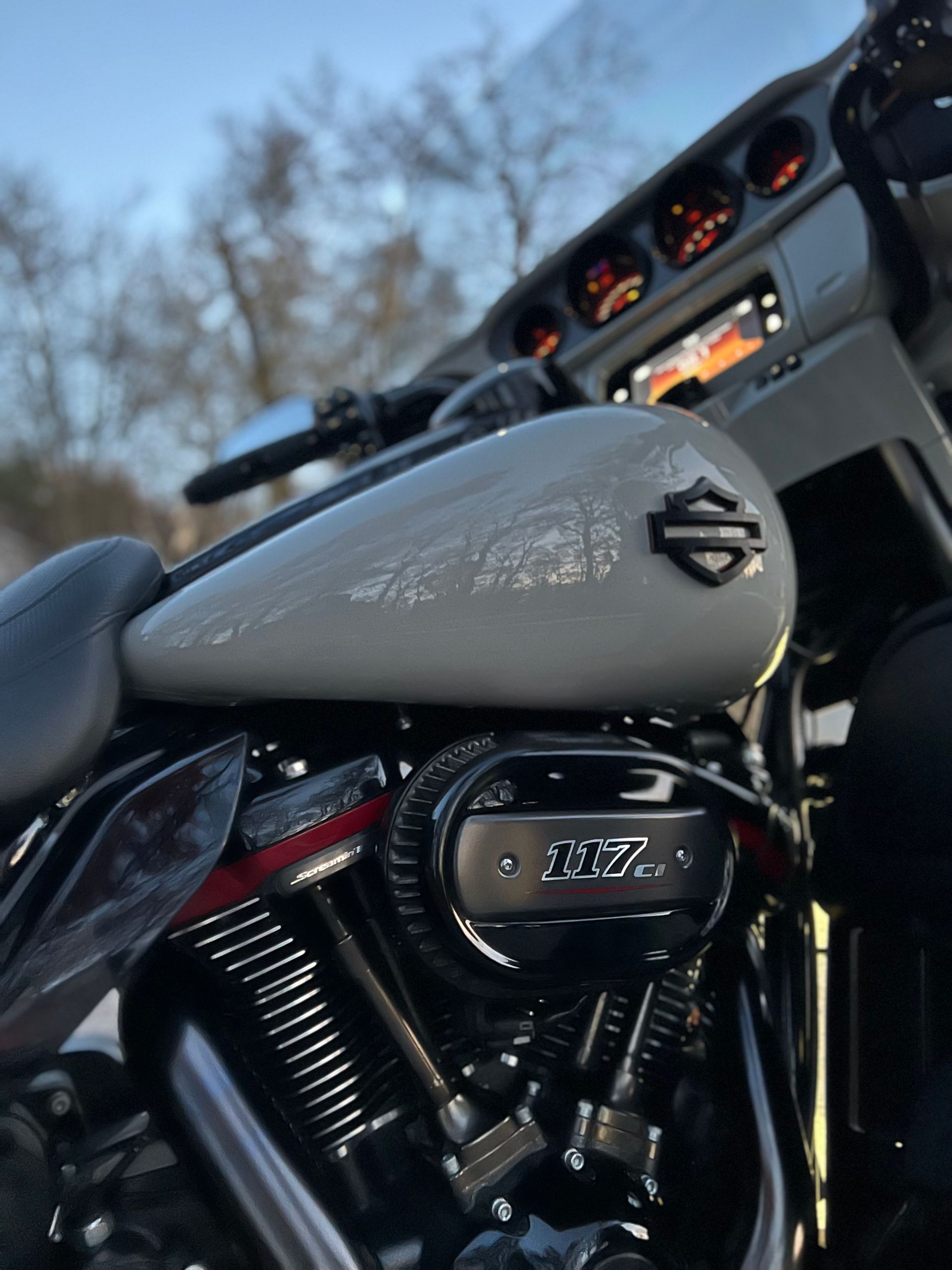 Close-up of a gray Harley-Davidson motorcycle seat and engine, with the dashboard glowing at dusk.