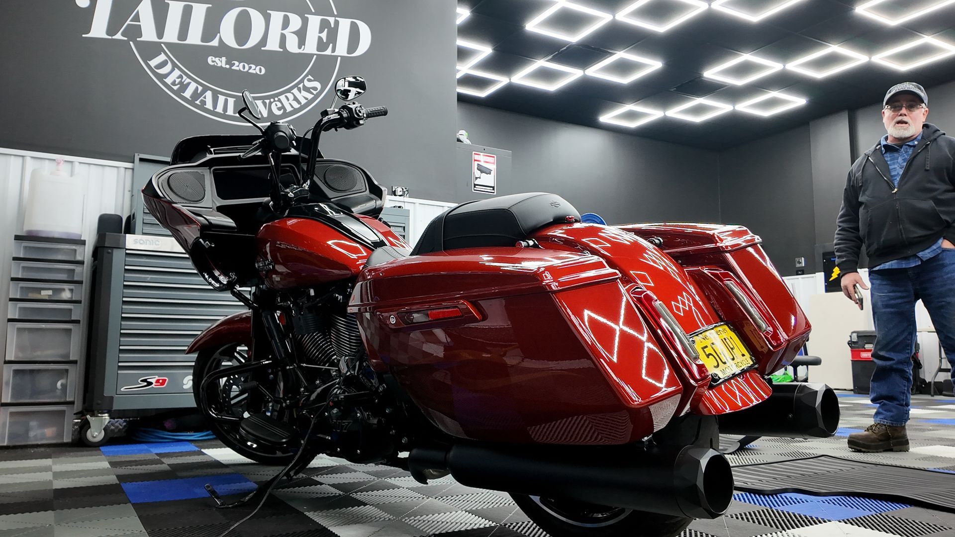 Red touring motorcycle in a workshop with a technician standing nearby under bright ceiling lights