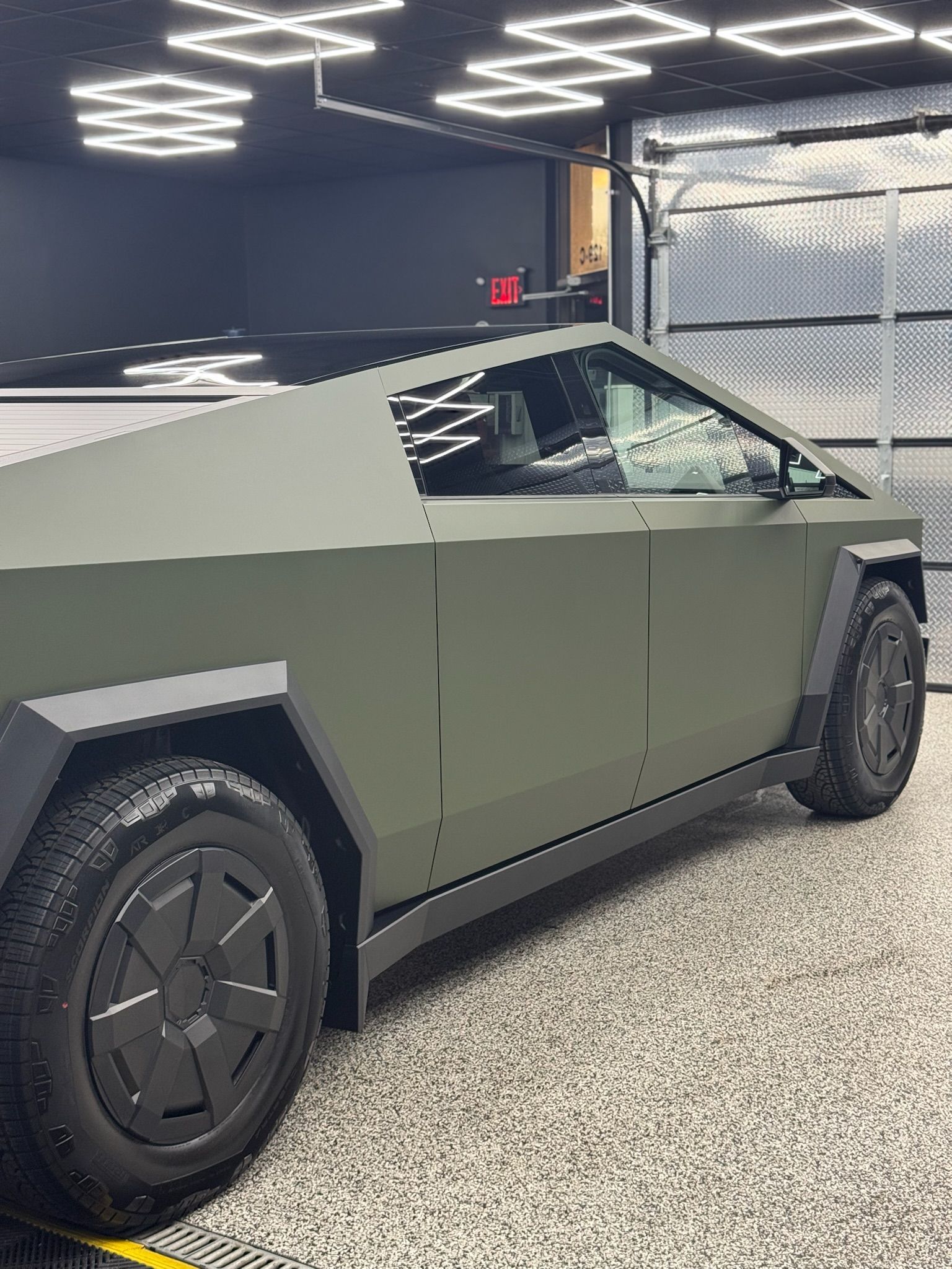 Matte olive-green Cybertruck parked indoors under geometric ceiling lights