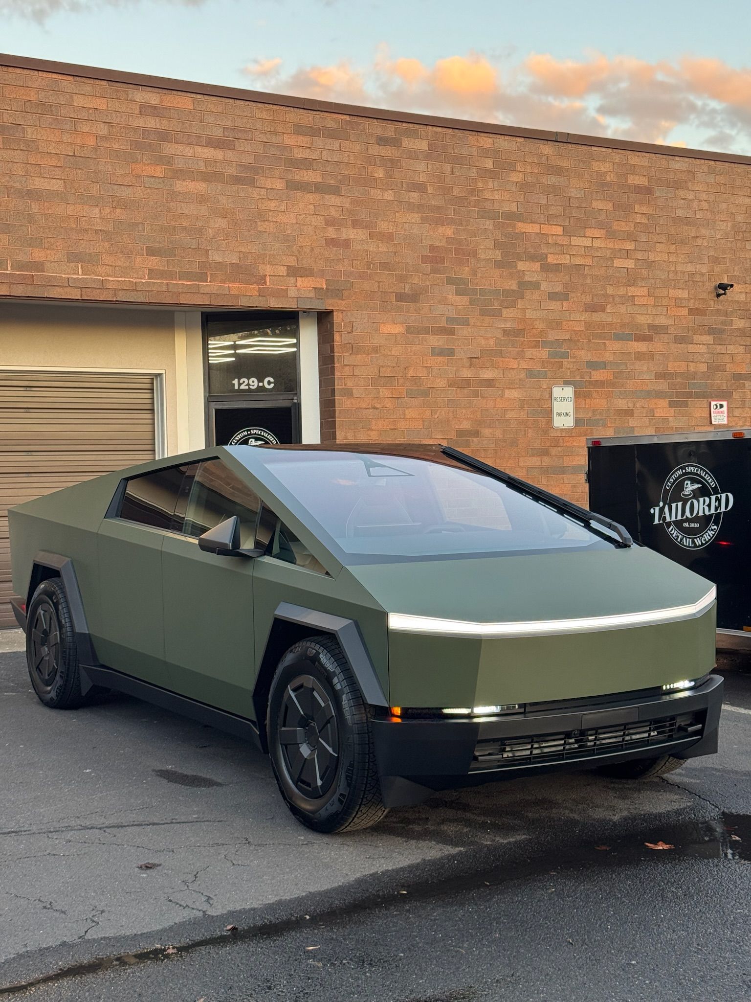 Olive-green Tesla Cybertruck parked by a brick building on a city street