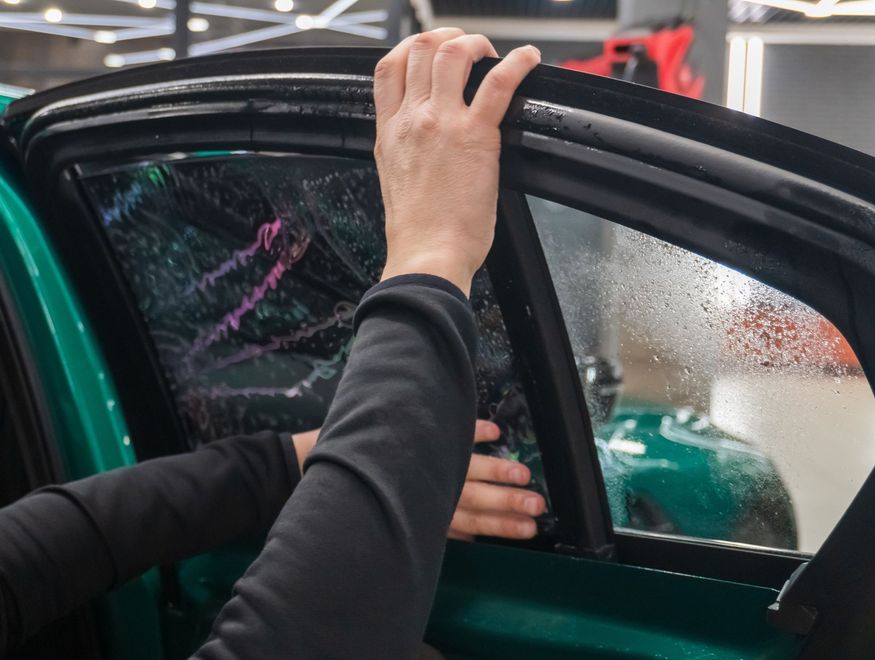Person opening a car door at an indoor auto show, with water droplets on the window