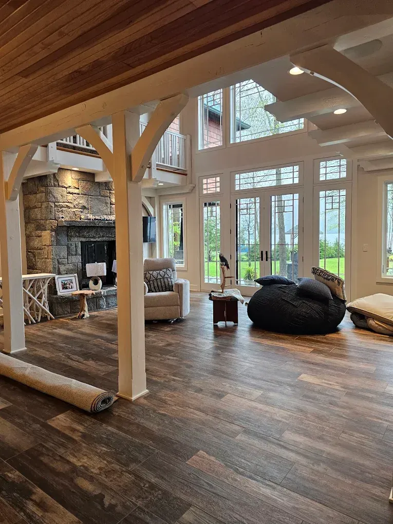 Spacious interior with exposed beams, stone fireplace, and large windows overlooking a scenic view.