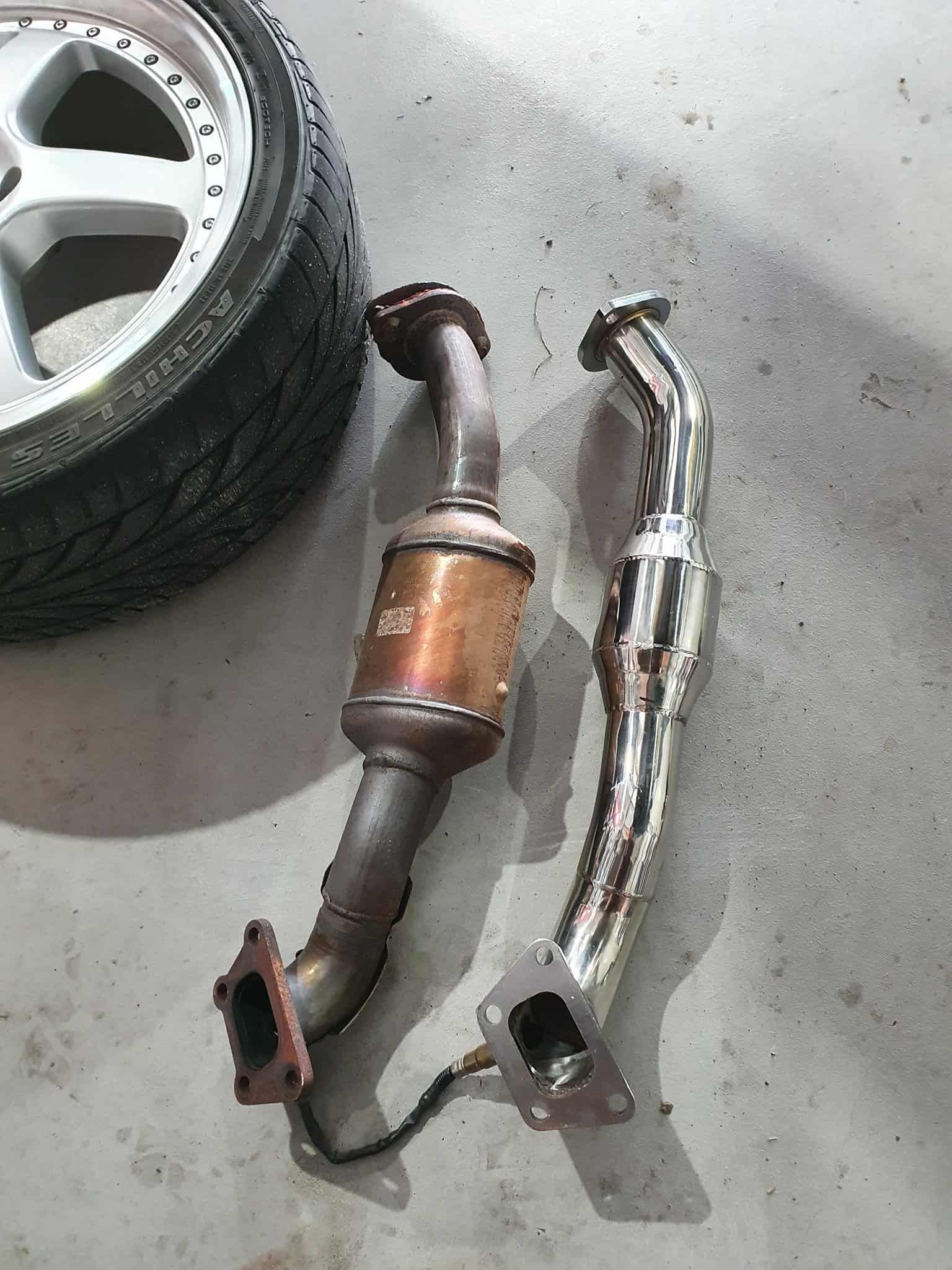 A Catalytic Converter and Exhaust Pipe Are Sitting on the Ground Next to a Tire — OSP Automotive & Marine In Grafton, NSW