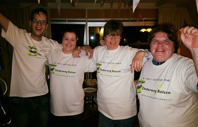 Vier lachende mensen in witte shirts poseren samen binnen, met hun armen om elkaar heen.