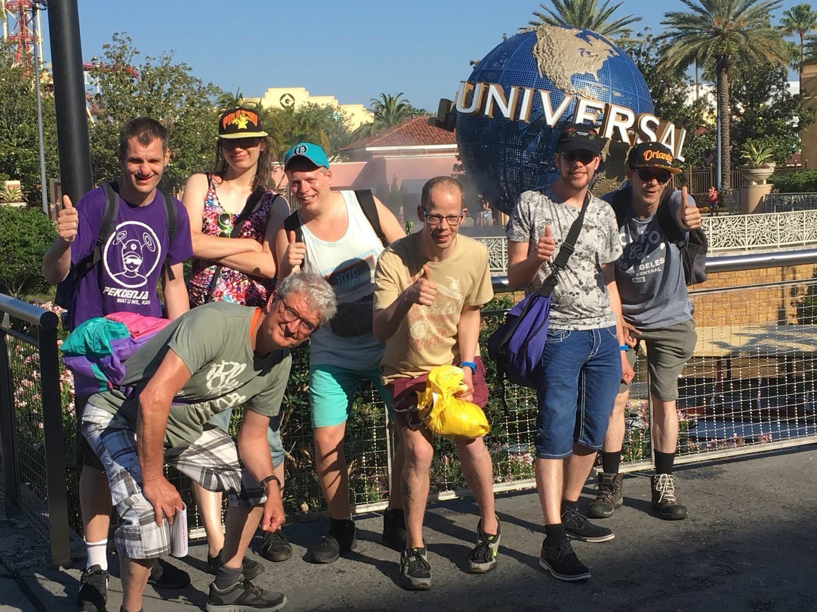 Een groep mensen poseert bij de ingang van Universal Studios, met een man in een felgele korte broek vooraan.