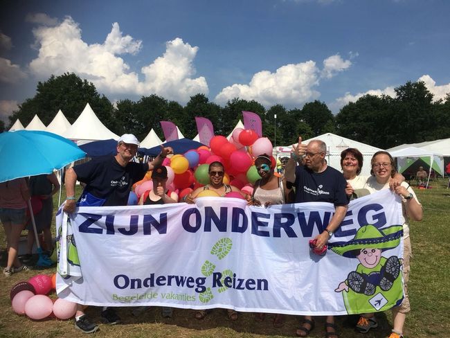 Mensen met een spandoek en ballonnen tijdens een buitenevenement onder een blauwe hemel.