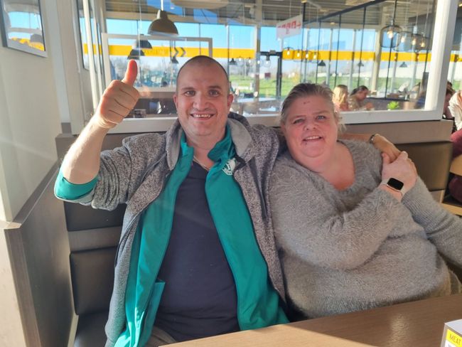 Drie mensen staan ​​lachend en elkaar omhelzend voor een deuropening, waarvan er één een duim omhoog steekt.