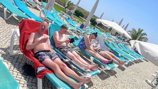 Een groep mensen steekt hun armen omhoog terwijl ze in het turquoise oceaanwater bij een strand drijven.