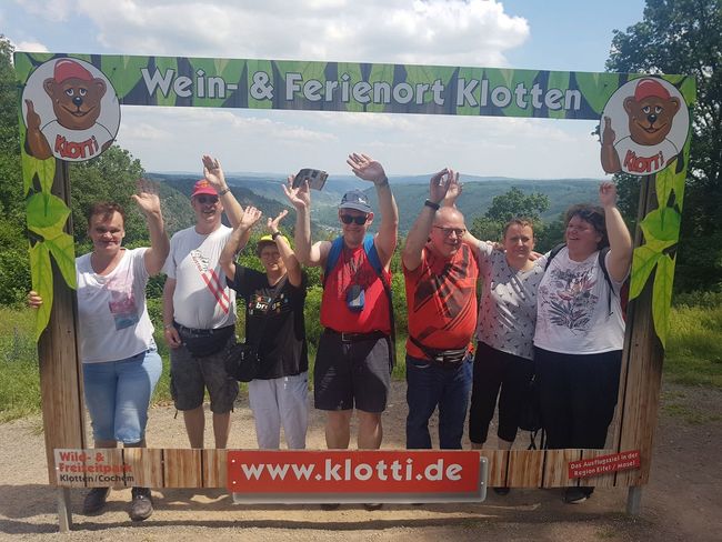 Een groep mensen poseert en juicht onder een festivalboog van 