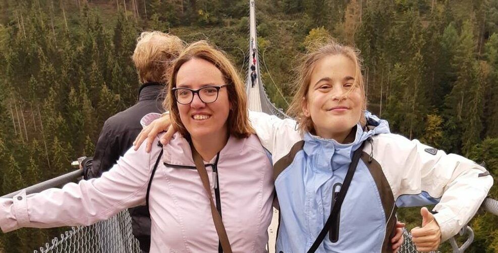 Twee mensen glimlachen met uitgestrekte armen op een bebost bergpad.