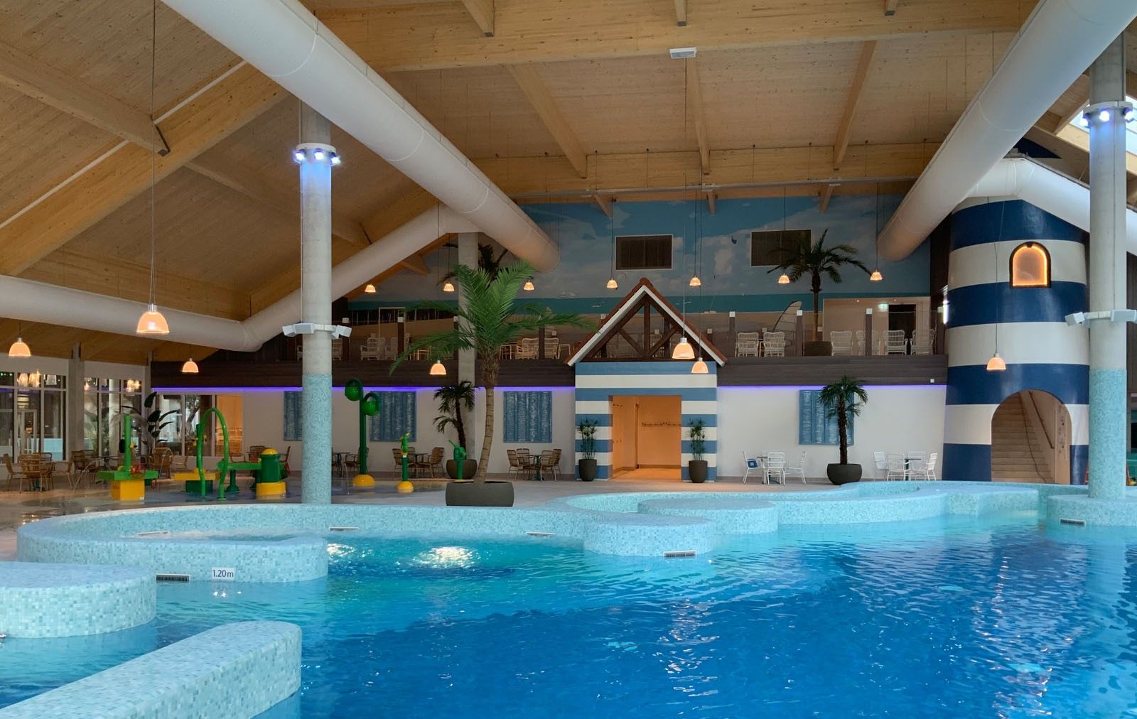 Binnenzwembad met helderblauw water, loungegedeelte en houten plafondbalken.
