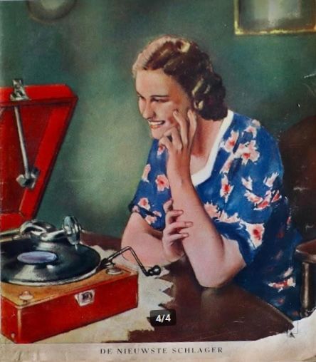 Een vrouw glimlacht naast een rode platenspeler en kijkt naar een draaiende vinylplaat op een tafel.