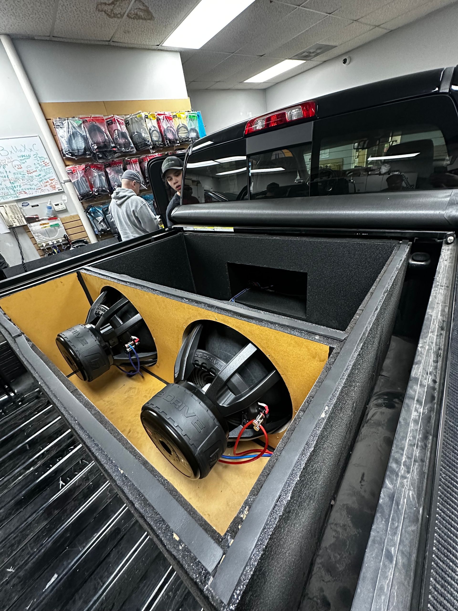 Truck bed with large black speakers mounted on a yellow panel in a store showroom