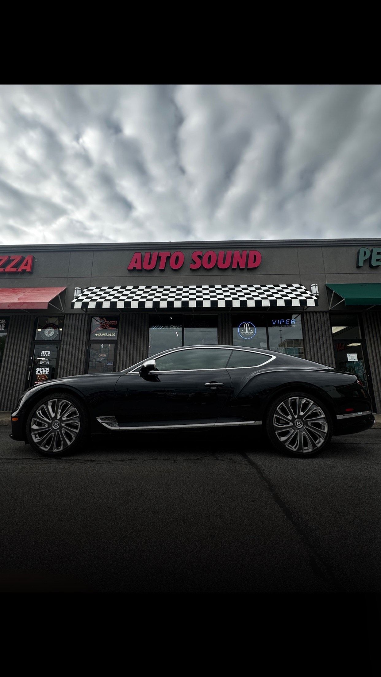 Black coupe parked outside an auto center under a cloudy sky