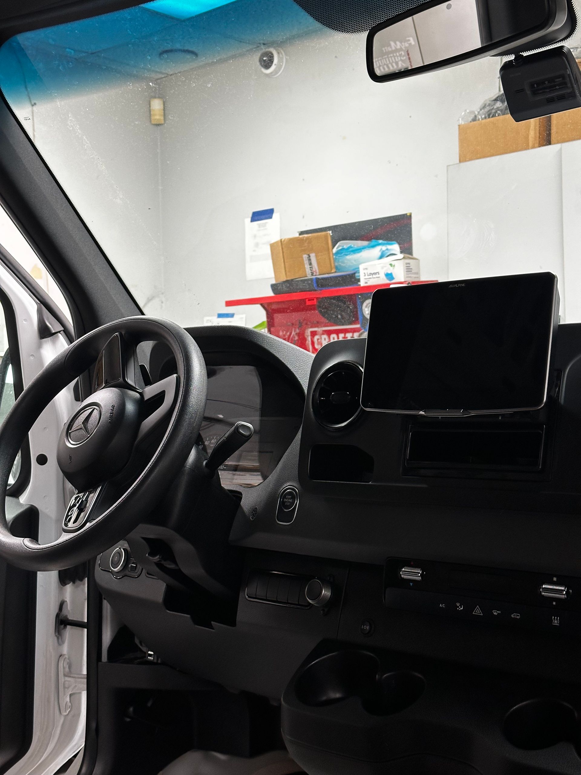 Car interior with steering wheel, dashboard, and center screen in a garage or workshop.