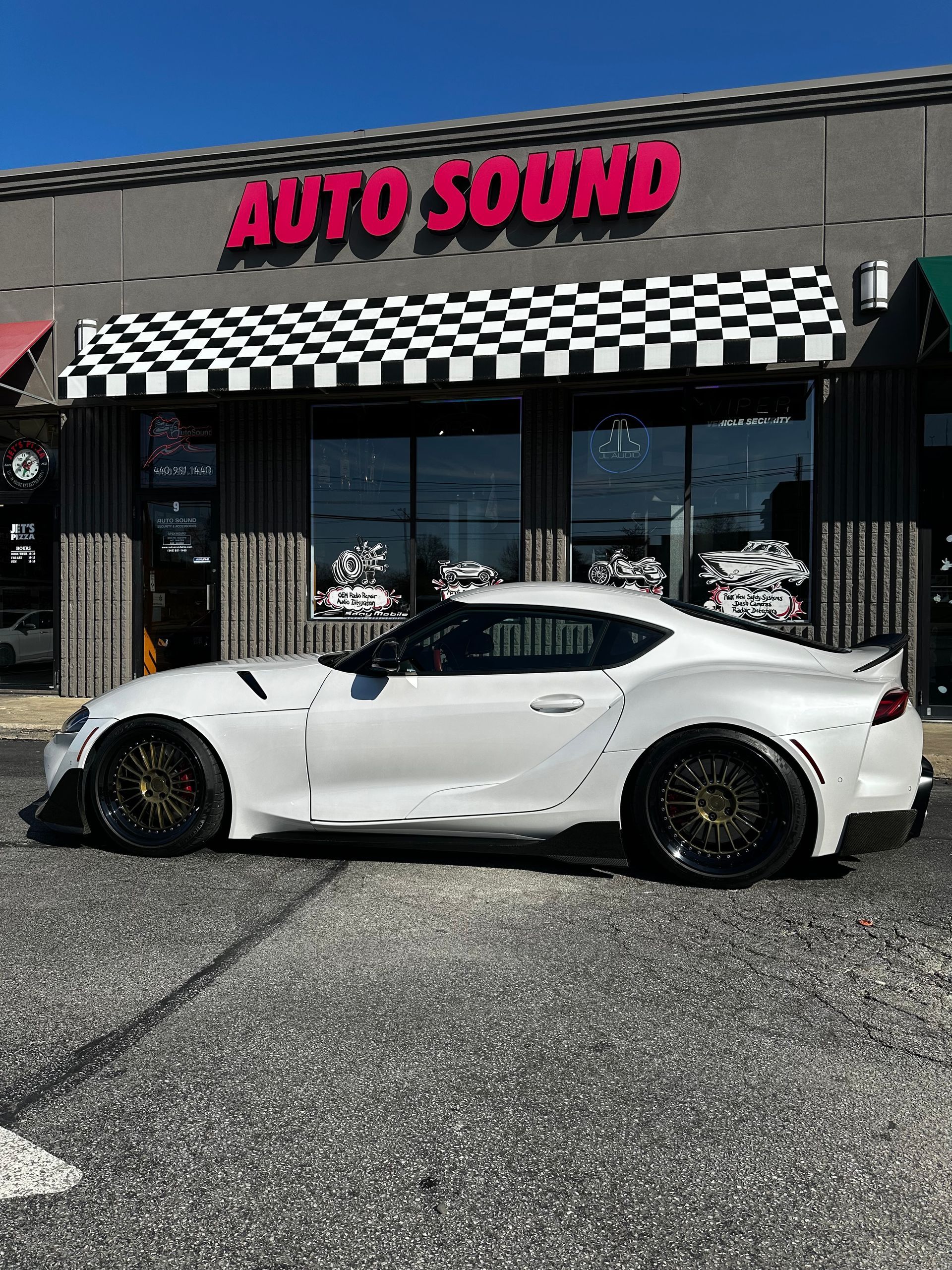 White sports car parked outside Auto Sound shop under a checkered awning