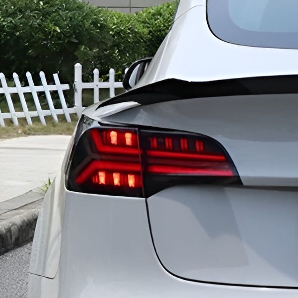 Close-up of a silver car’s rear taillight glowing red beside a white picket fence