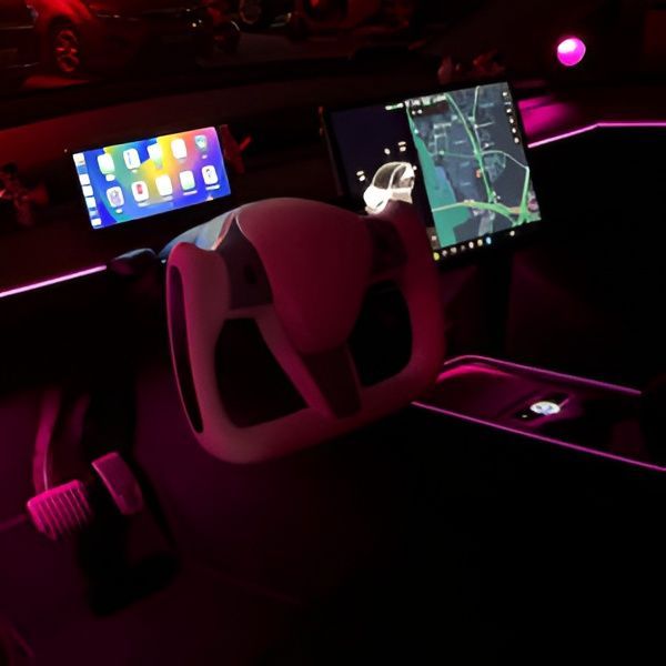 Neon-lit car interior with dual screens, pink accent lighting, and steering wheel view