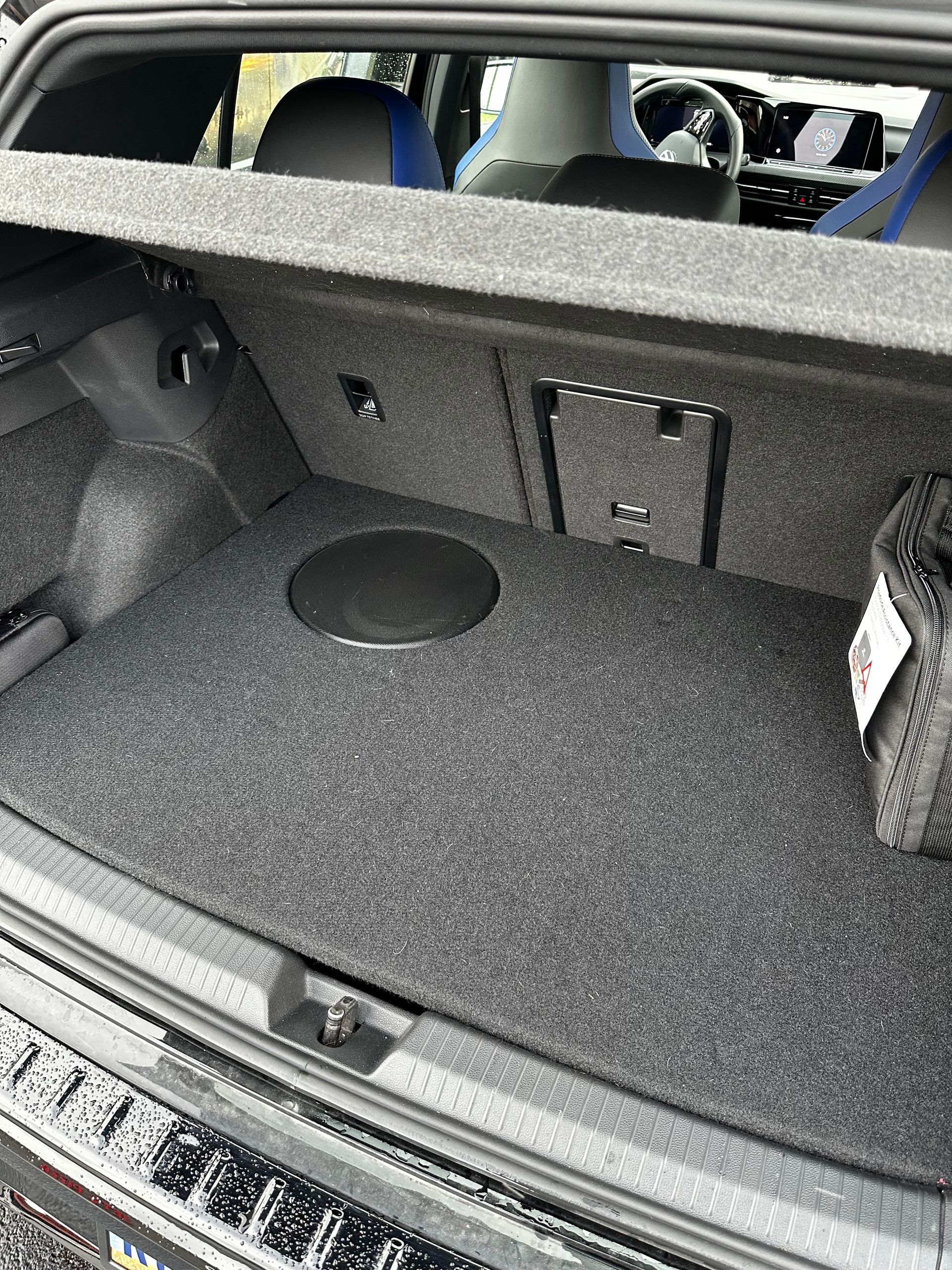 Car trunk with black carpeted cargo area, fold-down rear seats, and a speaker panel on the left side.