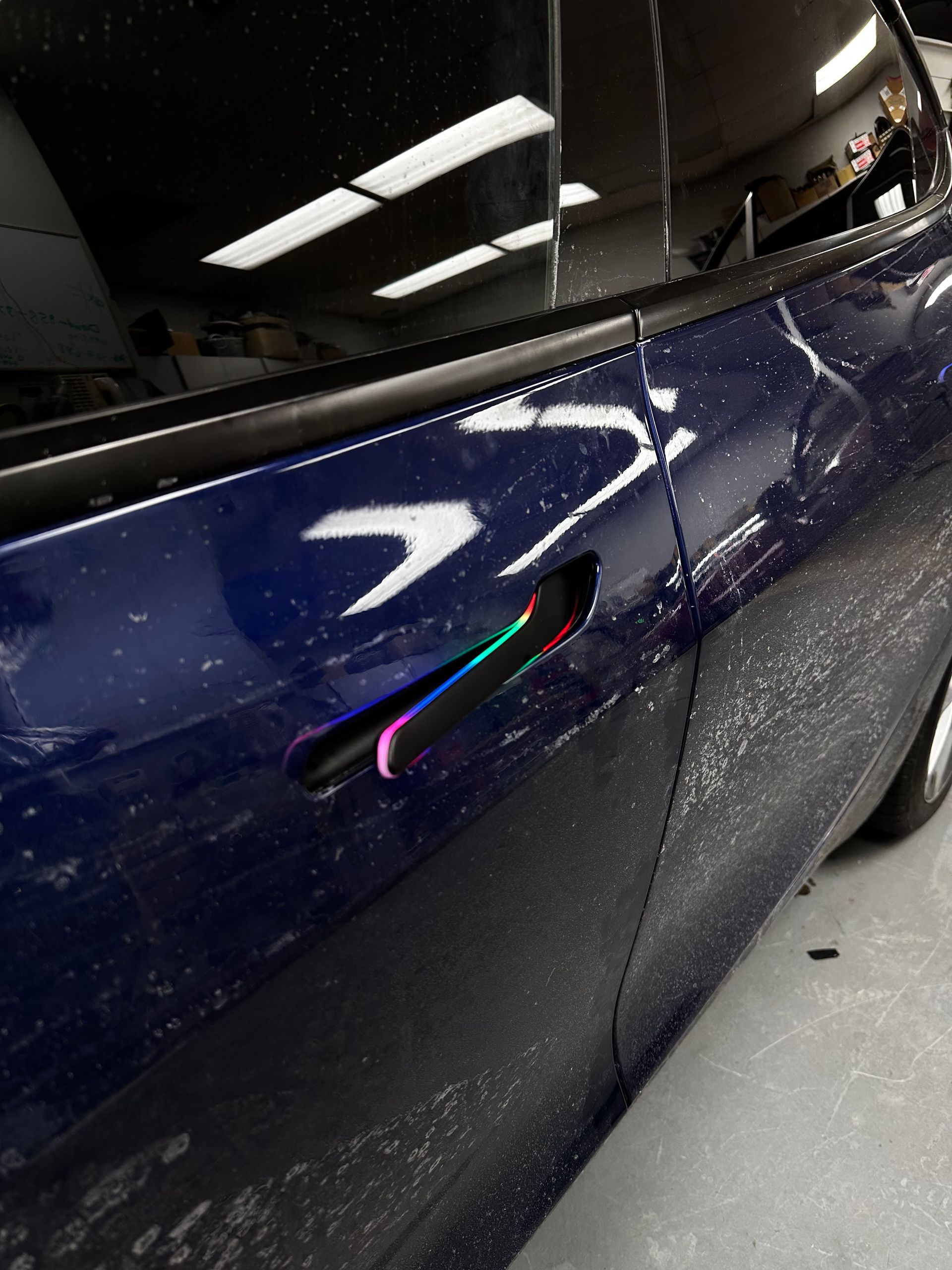 Close-up of a dark blue car door with a flush handle and glossy reflections in a garage